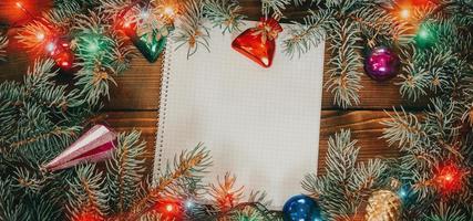 fondo de navidad con cuaderno en blanco para lista de tareas pendientes o lista de deseos. con ramas de abeto de navidad, adornos y regalo foto