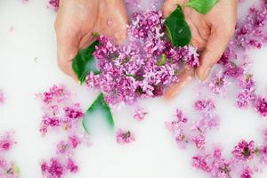 Young hands hold lilac petals in a milk bath. photo