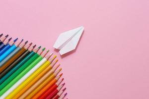 Paper plane, wood colored pencils, flat dip on pink background, top view. photo