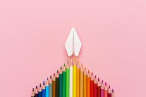 Paper plane, wood colored pencils, flat dip on pink background, top view. photo