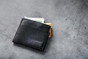 A black wallet with banknotes and a gold electronic card on a dark gray stone background. photo