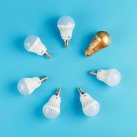 A Golden light bulb stands out in the circle of light bulbs of a ring of white lamps on a blue background. photo