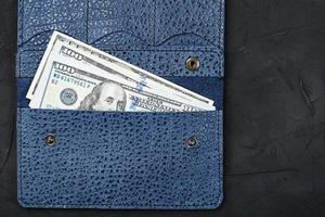 partmane de color azul de cuero genuino con nuevos billetes de cien dólares sobre un fondo negro. foto