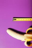 Yellow banana penis concept measured by measuring tape on pink background. Comparison of the size of a man's dignity. photo