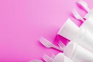 Disposable white plastic tableware on a pink background. photo