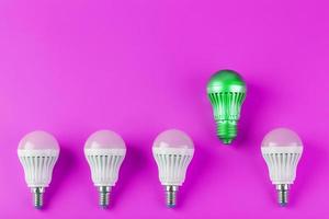 A special Light bulb stands out from the group of ordinary white light bulbs on a pink background. photo