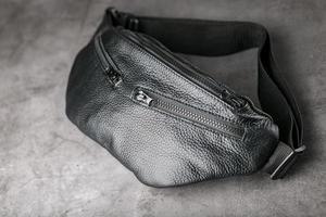 Belt bag made of textured black leather, banana on a gray background. photo