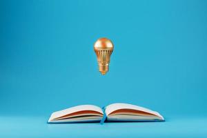 A Golden light bulb in levitation from an open notebook on a blue background. Concept of the idea. photo