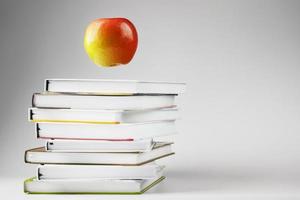 A red Apple hovers over a stack of books on a light background. photo