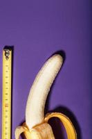 A banana is measured using a yellow ruler on a purple background. Adult material photo