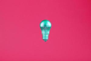 The light bulb hovers in the center of the frame in an isolated space on a pink background. photo