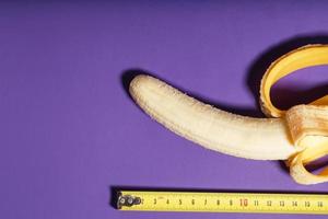 A banana is measured using a yellow ruler on a purple background. Adult material photo