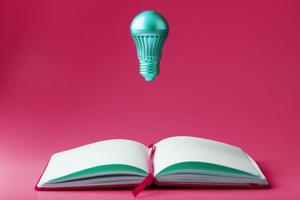 The light bulb hovers over the open pages of an empty notebook on a pink background. photo