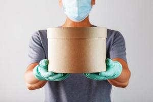 A delivery service courier in rubber gloves and a mask holds the parcel. photo