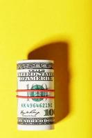 A roll of American bills with the shadow of an oil barrel on a yellow background. photo
