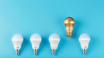 One gold led light bulb is higher and stands out from a row of white lamps on a blue background. photo