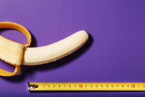 A peeled Banana is measured in length using a yellow ruler on a purple background. photo