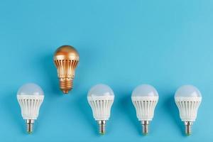 Gold light bulb is higher and stands out from a row of white lamps on a blue background. photo