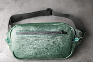 Belt bag made of dark green textured leather, banana on a gray background. photo