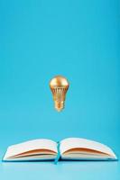 A Golden light bulb in levitation from an open notebook on a blue background. Concept of the idea. photo