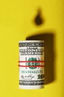 A roll of American bills with the shadow of an oil barrel and a drop of oil on a yellow background. photo