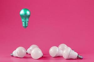 una bombilla especial se cierne sobre simples bombillas de luz blanca estándar sobre un fondo rosa. foto