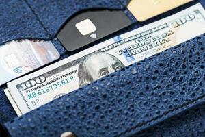 monedero azul con billetes y tarjetas de crédito en un fondo negro. foto