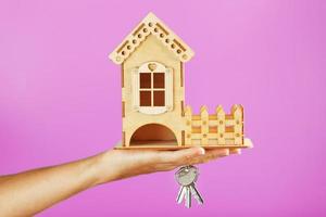 A small wooden house with keys in hand on a pink background. photo