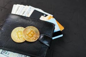 A black wallet with dollars, e-cards and bitcoins on a black textured background. photo