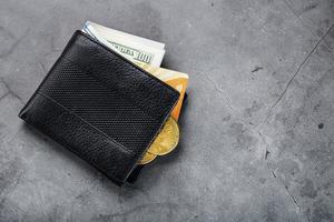 A black wallet with banknotes and a gold electronic card on a dark gray stone background. photo