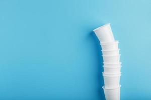 Plastic cups of disposable tableware in the shape of a tower on a blue background. photo