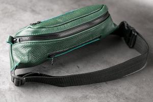 Belt bag made of dark green textured leather, banana on a gray background. photo