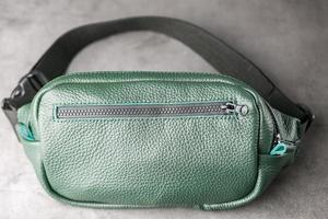 Belt bag made of dark green textured leather, banana on a gray background. photo