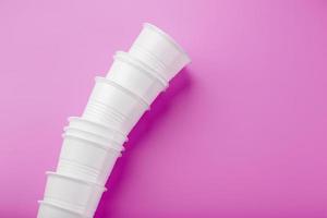 Disposable white plastic tableware glasses in a row, on a pink background. photo