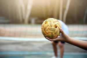 Sepak takraw ball, southeast asian countries traditional sport, holding in hand of young asian female sepak takraw player in front of the net before throwing it to another player to kick over the net. photo