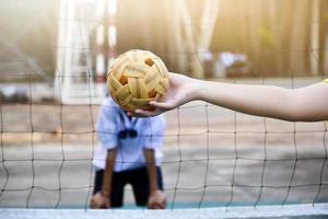 pelota de sepak takraw, deporte tradicional de los países del sudeste asiático, sosteniendo en la mano a una joven jugadora asiática de sepak takraw frente a la red antes de arrojársela a otro jugador para que patee la red. foto