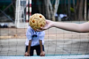 pelota de sepak takraw, deporte tradicional de los países del sudeste asiático, sosteniendo en la mano a una joven jugadora asiática de sepak takraw frente a la red antes de arrojársela a otro jugador para que patee la red. foto