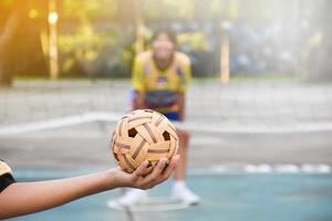 pelota de sepak takraw, deporte tradicional de los países del sudeste asiático, sosteniendo en la mano a una joven jugadora asiática de sepak takraw frente a la red antes de arrojársela a otro jugador para que patee la red. foto