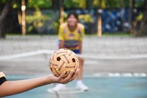 pelota de sepak takraw, deporte tradicional de los países del sudeste asiático, sosteniendo en la mano a una joven jugadora asiática de sepak takraw frente a la red antes de arrojársela a otro jugador para que patee la red. foto