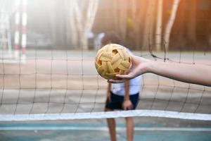 pelota de sepak takraw, deporte tradicional de los países del sudeste asiático, sosteniendo en la mano a una joven jugadora asiática de sepak takraw frente a la red antes de arrojársela a otro jugador para que patee la red. foto