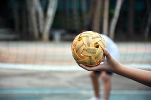 pelota de sepak takraw, deporte tradicional de los países del sudeste asiático, sosteniendo en la mano a una joven jugadora asiática de sepak takraw frente a la red antes de arrojársela a otro jugador para que patee la red.