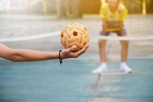 pelota de sepak takraw, deporte tradicional de los países del sudeste asiático, sosteniendo en la mano a una joven jugadora asiática de sepak takraw frente a la red antes de arrojársela a otro jugador para que patee la red. foto