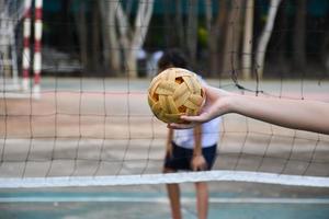 pelota de sepak takraw, deporte tradicional de los países del sudeste asiático, sosteniendo en la mano a una joven jugadora asiática de sepak takraw frente a la red antes de arrojársela a otro jugador para que patee la red. foto