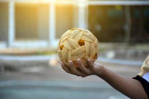 pelota de sepak takraw, deporte tradicional de los países del sudeste asiático, sosteniendo en la mano a una joven jugadora asiática de sepak takraw frente a la red antes de arrojársela a otro jugador para que patee la red. foto