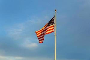 bandera americana en asta de bandera ondeando el viento contra las nubes, cielo azul foto