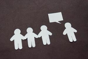 Silhouettes of people cut from white paper on a black background. A group of people stands in front of one person who is speaking speech-bubble. Communication, leadership, teamwork concept photo