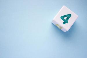 Close-up photo of a white plastic cube with a green number 4 on a blue background in the upper right corner. With copy space