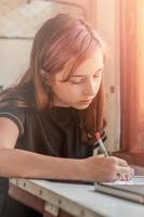 A teenage girl rides a train. The girl writes with a pencil in a notebook. photo