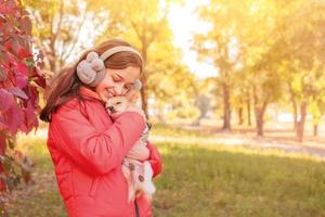 una adolescente con una chaqueta naranja con un perro chihuahua en los brazos. la niña abraza a su perro.