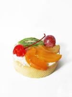 pastel con crema, cereza, uvas, kiwi en rodajas y mango sobre un fondo blanco foto